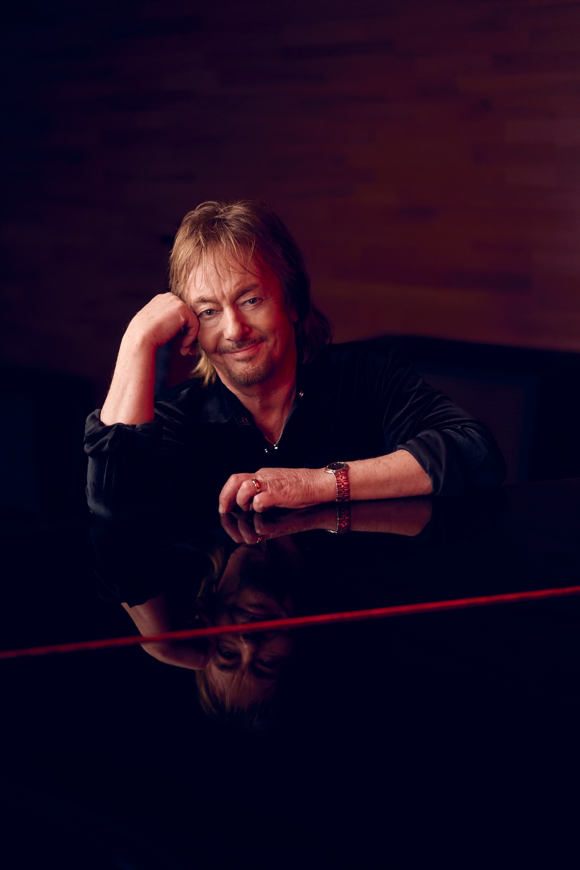 Chris Norman sits at a black grand piano in which he sees his reflection.